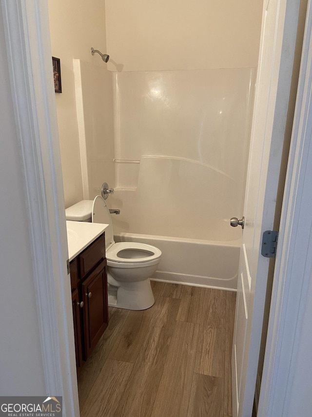 bathroom featuring toilet,  shower combination, wood finished floors, and vanity