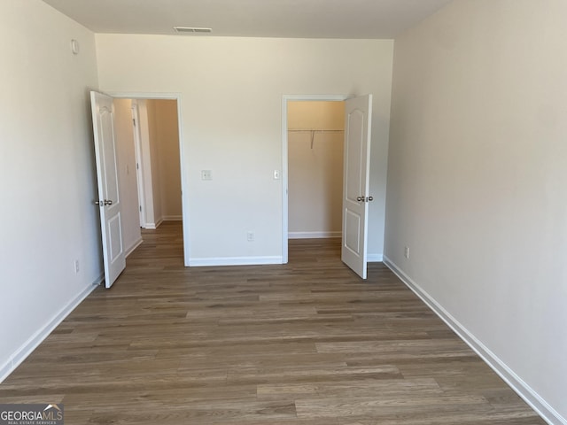 unfurnished bedroom featuring baseboards, a spacious closet, visible vents, and wood finished floors