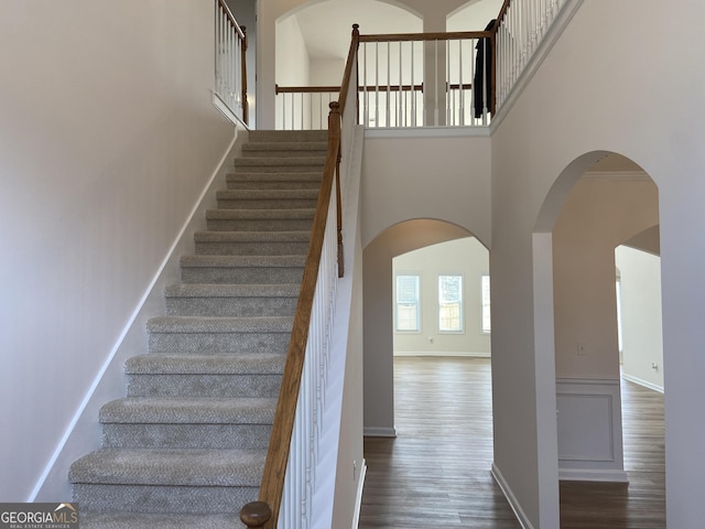 stairway featuring arched walkways, wood finished floors, a towering ceiling, and baseboards