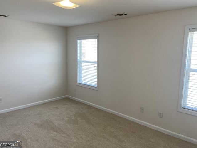 spare room with light carpet, visible vents, and baseboards