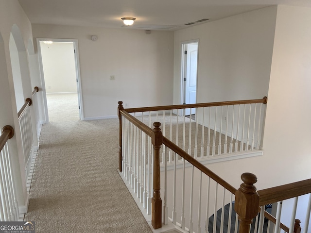 hallway featuring carpet, baseboards, visible vents, and an upstairs landing