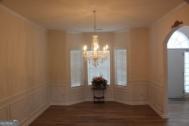 unfurnished dining area with an inviting chandelier, arched walkways, dark wood finished floors, and crown molding