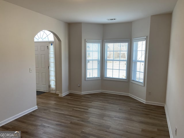 foyer with arched walkways, dark wood-type flooring, visible vents, and baseboards