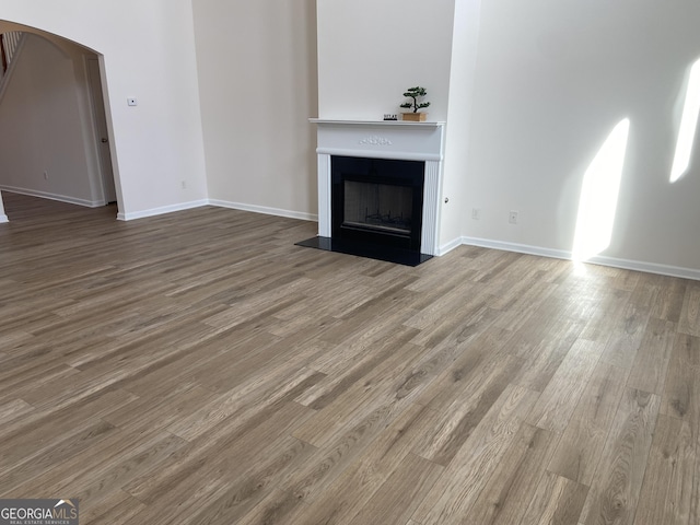 unfurnished living room featuring arched walkways, wood finished floors, a fireplace with flush hearth, and baseboards