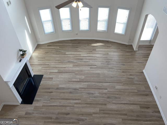 unfurnished living room with ceiling fan, arched walkways, and wood finished floors