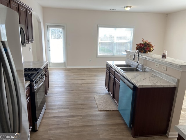 kitchen featuring light wood-style flooring, a kitchen island with sink, a sink, dark brown cabinets, and appliances with stainless steel finishes