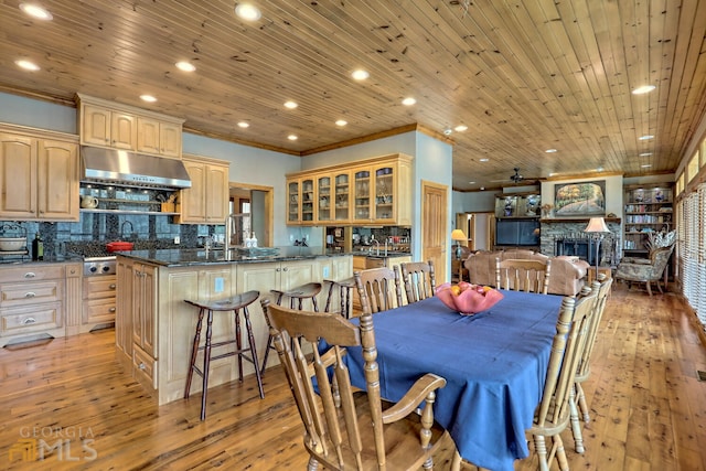 dining area featuring crown molding, light wood-type flooring, a fireplace, and wooden ceiling