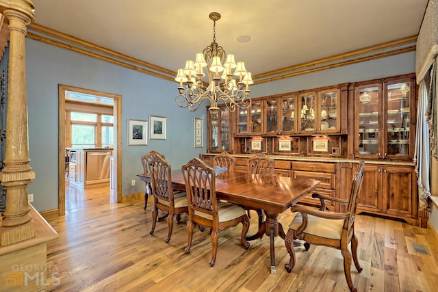 dining area featuring light wood-type flooring, ornate columns, ornamental molding, and an inviting chandelier