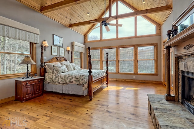 bedroom featuring beamed ceiling, light hardwood / wood-style floors, a stone fireplace, and wooden ceiling