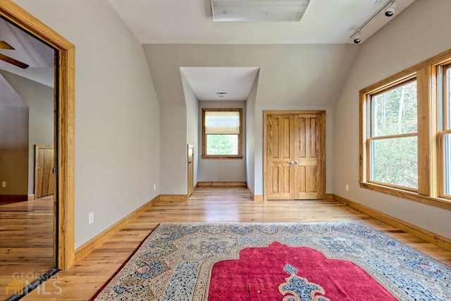 interior space with light wood-type flooring, rail lighting, and vaulted ceiling