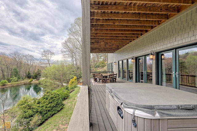 wooden deck with a water view and a hot tub