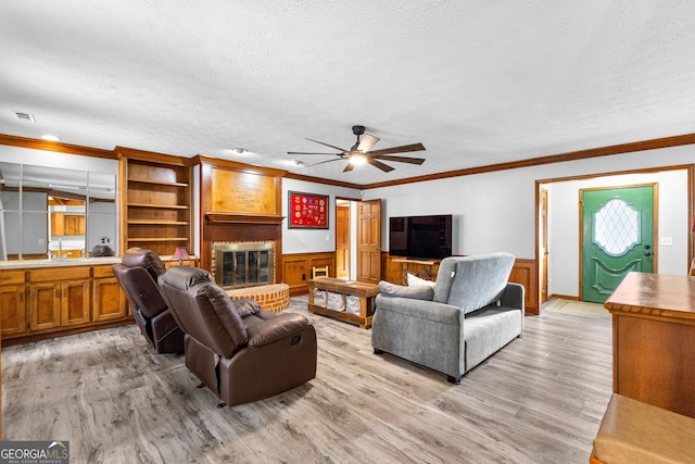 living room with ceiling fan, a brick fireplace, ornamental molding, a textured ceiling, and light wood-type flooring