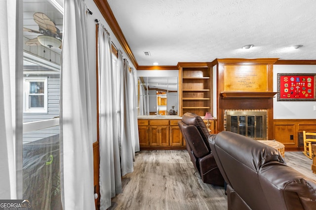 living room featuring a textured ceiling, light wood-type flooring, and ornamental molding