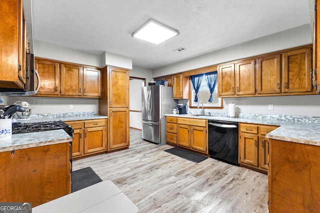 kitchen featuring a textured ceiling, sink, light wood-type flooring, and stainless steel appliances