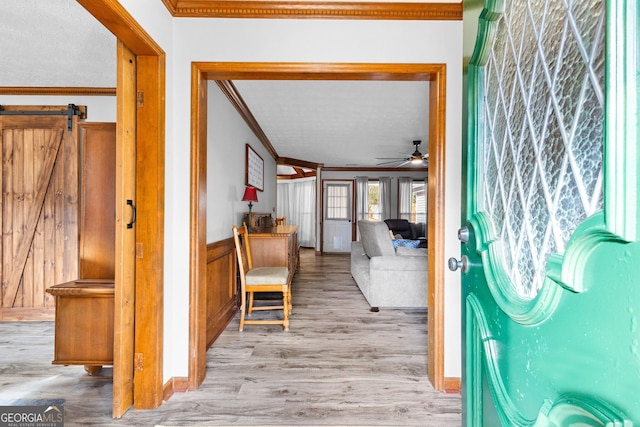 corridor featuring a barn door, light hardwood / wood-style flooring, and ornamental molding