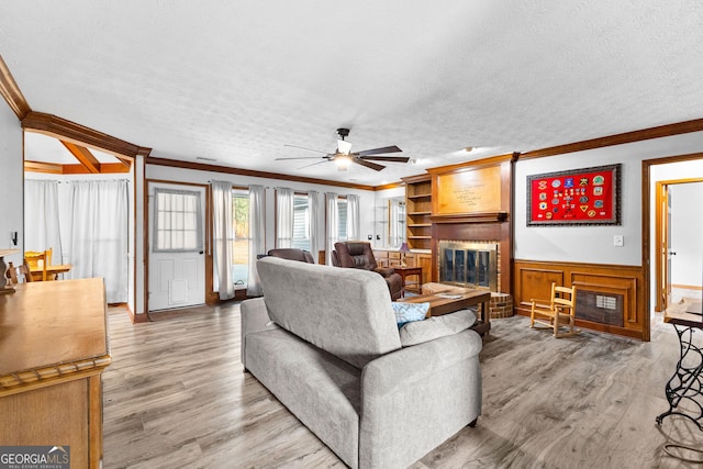 living room with crown molding, ceiling fan, a textured ceiling, and a brick fireplace