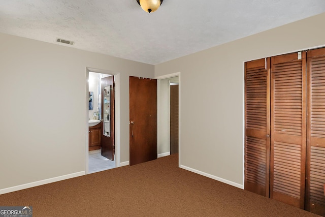 unfurnished bedroom featuring carpet, ensuite bathroom, a textured ceiling, and a closet