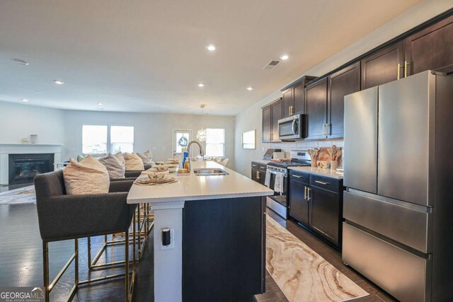 kitchen featuring appliances with stainless steel finishes, a breakfast bar, an island with sink, sink, and dark wood-type flooring