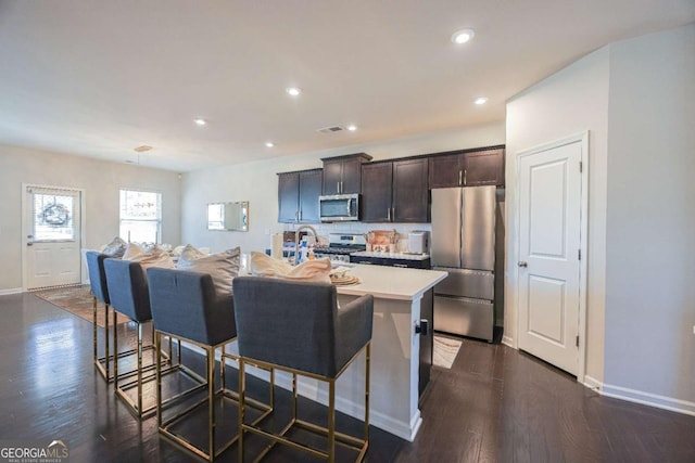 kitchen featuring a breakfast bar, dark brown cabinets, dark hardwood / wood-style flooring, an island with sink, and stainless steel appliances