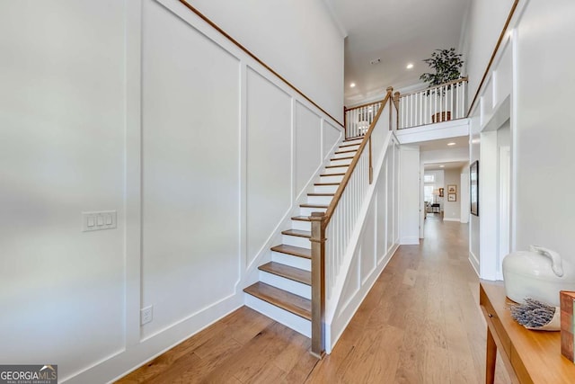 stairs with recessed lighting, baseboards, a high ceiling, and wood finished floors