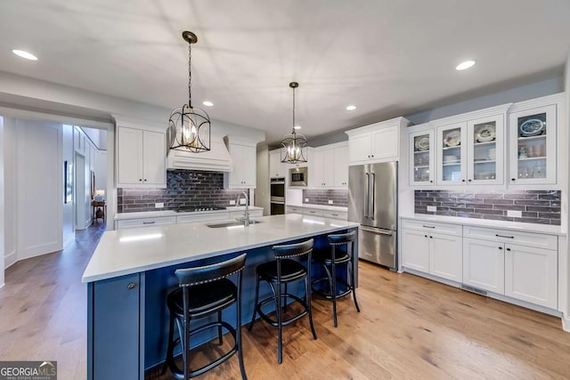 kitchen with stainless steel appliances, light countertops, hanging light fixtures, white cabinetry, and a sink