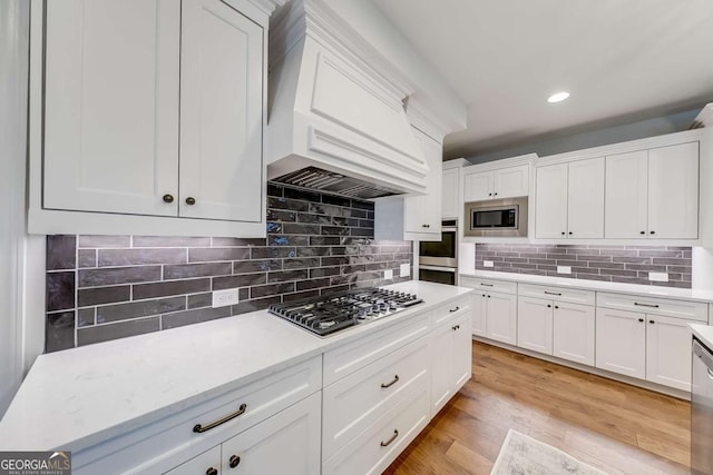 kitchen with premium range hood, light wood finished floors, white cabinets, appliances with stainless steel finishes, and tasteful backsplash