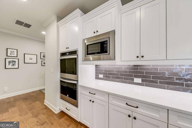 kitchen with stainless steel appliances, visible vents, white cabinetry, light countertops, and ornamental molding