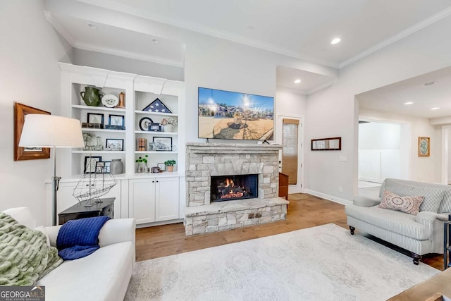 living area with light wood-style floors, baseboards, ornamental molding, and a stone fireplace