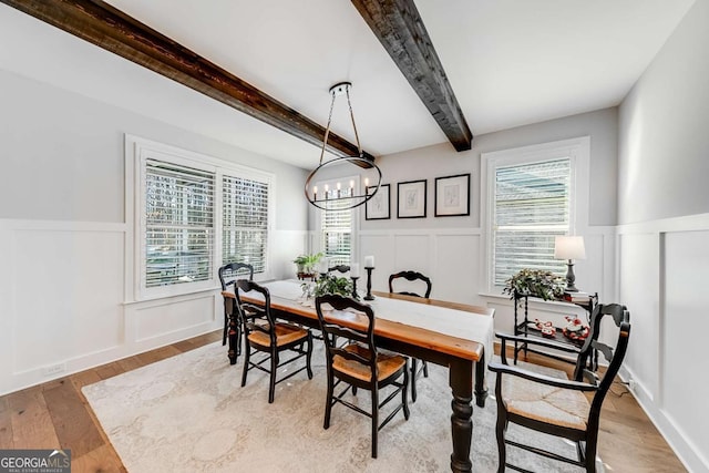 dining space with beamed ceiling, a decorative wall, a wainscoted wall, and wood finished floors