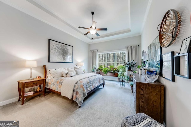 carpeted bedroom featuring a ceiling fan, a tray ceiling, and baseboards