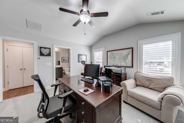 home office with light colored carpet, vaulted ceiling, a ceiling fan, and visible vents