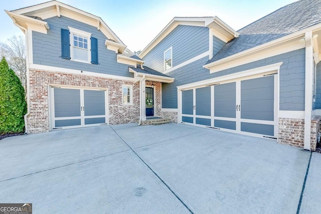 view of front facade featuring an attached garage, a shingled roof, concrete driveway, and brick siding