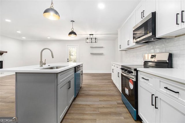 kitchen with appliances with stainless steel finishes, a kitchen island with sink, sink, pendant lighting, and white cabinets