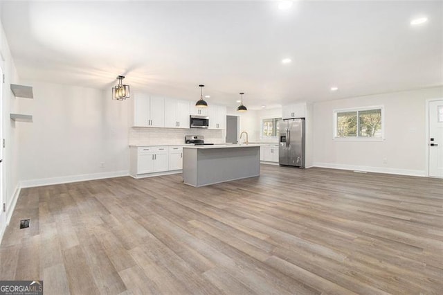 kitchen with stainless steel appliances, pendant lighting, white cabinets, light hardwood / wood-style floors, and an island with sink