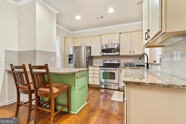 kitchen with a kitchen bar, appliances with stainless steel finishes, light stone countertops, sink, and a center island