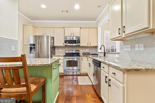 kitchen with light stone counters, sink, stainless steel appliances, and cream cabinets