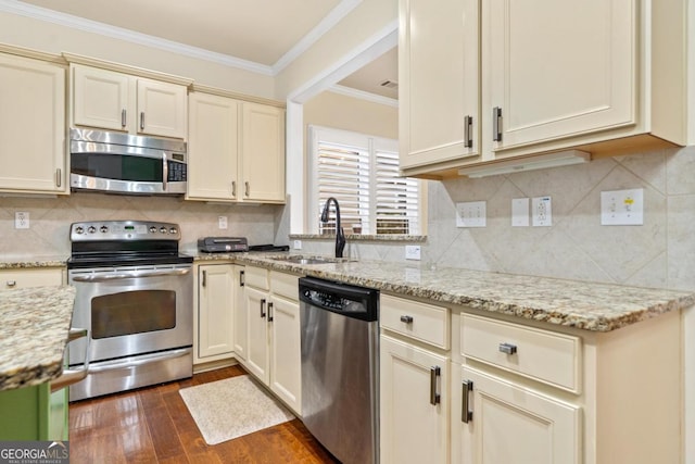 kitchen featuring sink, stainless steel appliances, light stone counters, cream cabinets, and ornamental molding