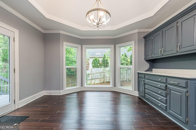 unfurnished dining area featuring a tray ceiling, dark hardwood / wood-style flooring, ornamental molding, and an inviting chandelier