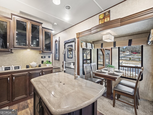 kitchen featuring dark brown cabinetry, a center island with sink, and dark wood-type flooring