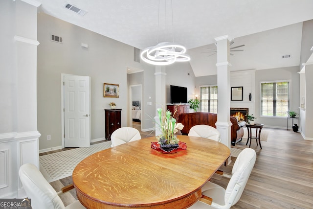 dining room featuring ceiling fan with notable chandelier, a large fireplace, light wood-type flooring, and a wealth of natural light