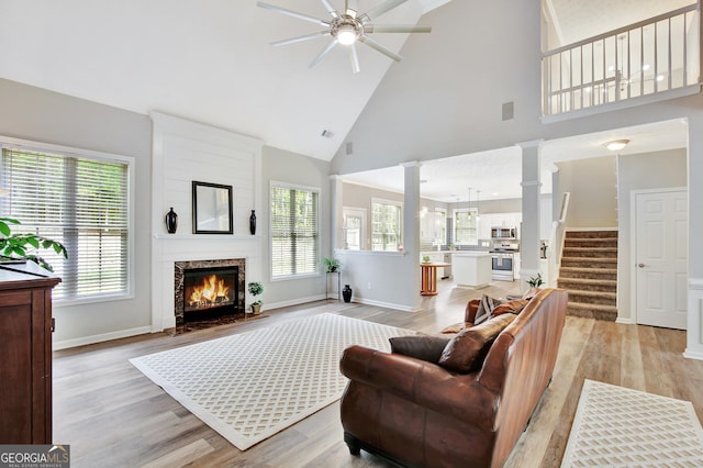 living room with ceiling fan, ornate columns, high vaulted ceiling, and light hardwood / wood-style flooring