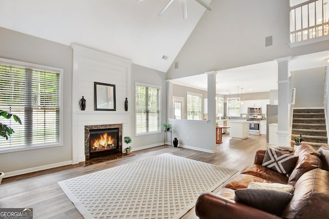 living room with ceiling fan, a premium fireplace, high vaulted ceiling, decorative columns, and light hardwood / wood-style floors