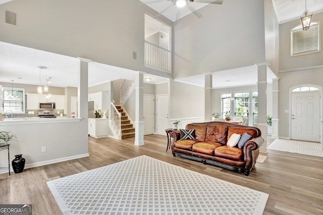 entrance foyer with ceiling fan with notable chandelier, light hardwood / wood-style floors, a high ceiling, and decorative columns