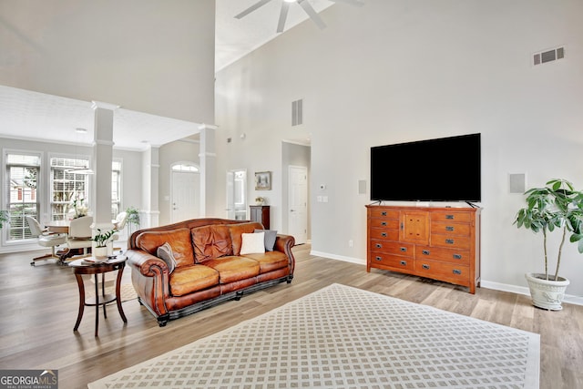 living room with ceiling fan, light hardwood / wood-style flooring, high vaulted ceiling, and decorative columns