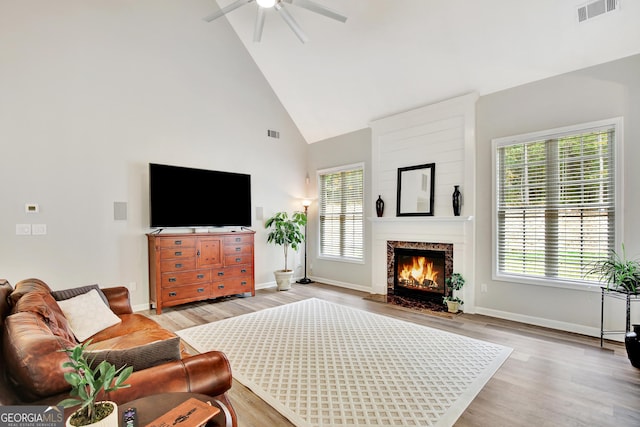 living room featuring a large fireplace, light hardwood / wood-style flooring, high vaulted ceiling, and ceiling fan