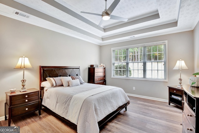 bedroom with a tray ceiling, ceiling fan, light hardwood / wood-style flooring, and ornamental molding