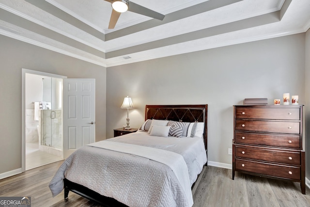 bedroom featuring ceiling fan, light hardwood / wood-style floors, a raised ceiling, and connected bathroom