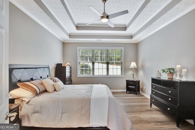 bedroom featuring a raised ceiling, crown molding, light hardwood / wood-style flooring, and ceiling fan