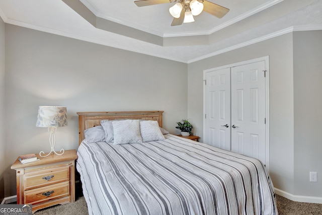 carpeted bedroom featuring a tray ceiling, ceiling fan, a closet, and crown molding