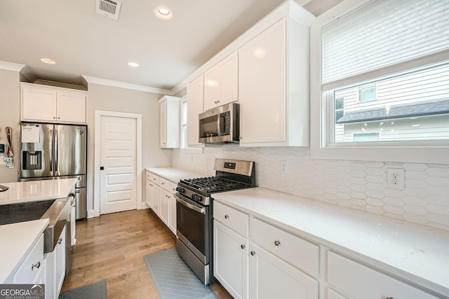 kitchen featuring white cabinetry, light hardwood / wood-style flooring, backsplash, appliances with stainless steel finishes, and ornamental molding